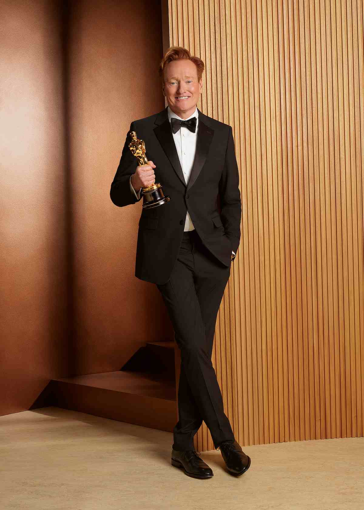 Conan O'Brien in a tuxedo as host holding an Oscar statue
