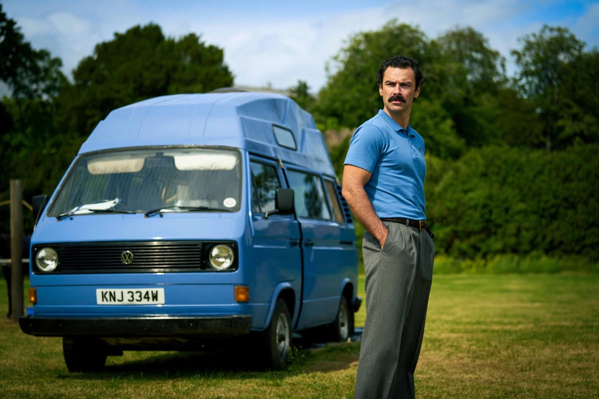 AIDAN TURNER in a blue shirt next to a blue van