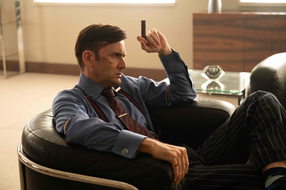 DAVID TENNANT in a suit and tie smoking a cigar and sitting in a lounge chair