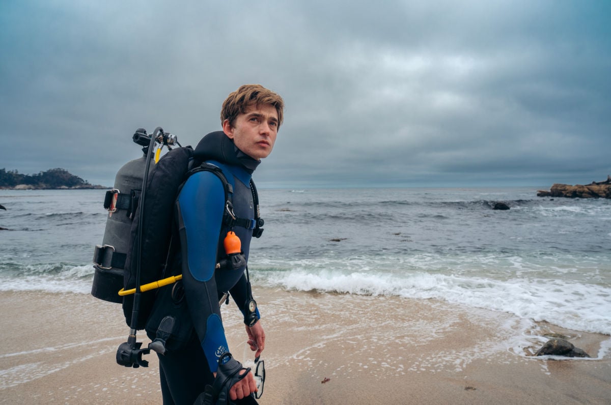 Austin Abrams in scuba diving gear on a beach