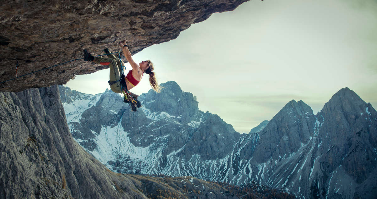 Lily James in climbing gear hanging off of a rock